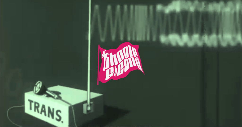 A frame from the 1944 US War Department film, BASIC PRINCIPLES OF FREQUENCY MODULATION, illustrating a frequency-modulation (FM) radio signal transmitter, labeled “TRANS.”, transmitting a signal. The Phoole and the Gang fuchsia flag logo is included.