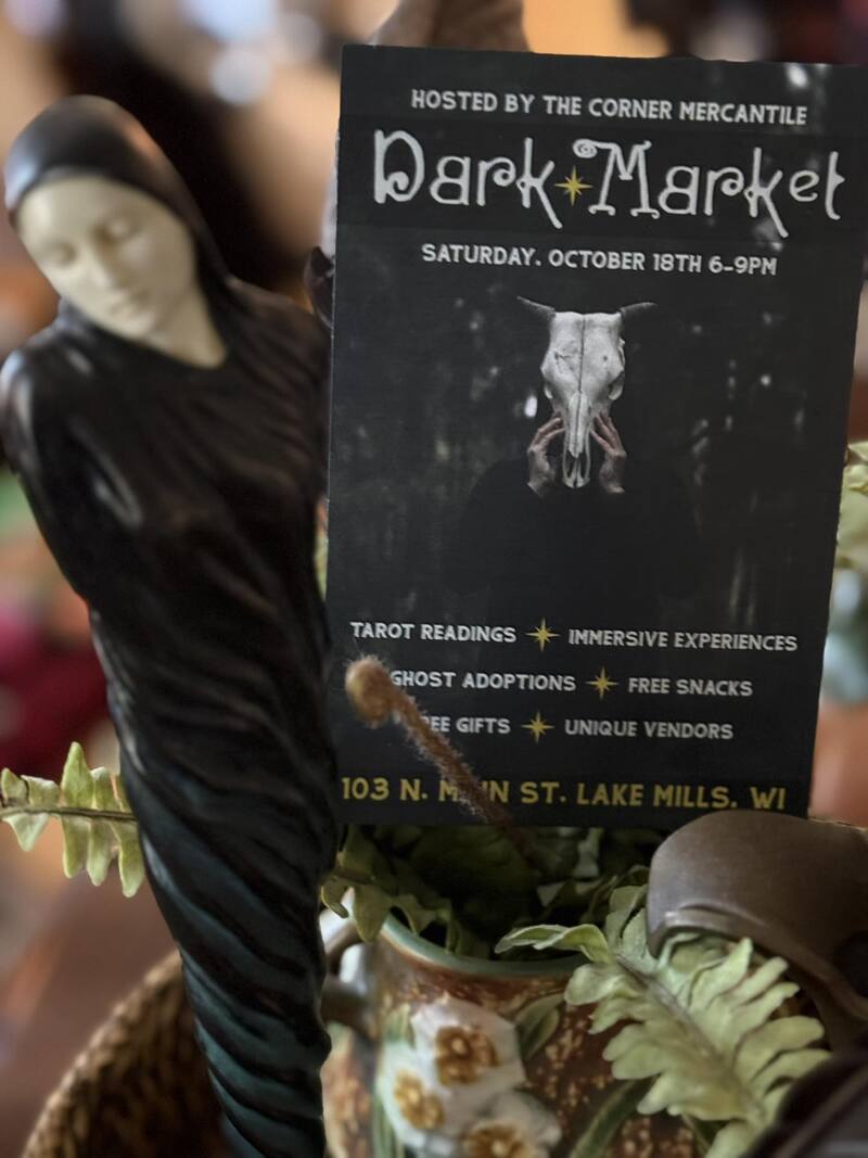 A postcard advertises the Dark Market, embraced by a ghoulish figurine in a fern.